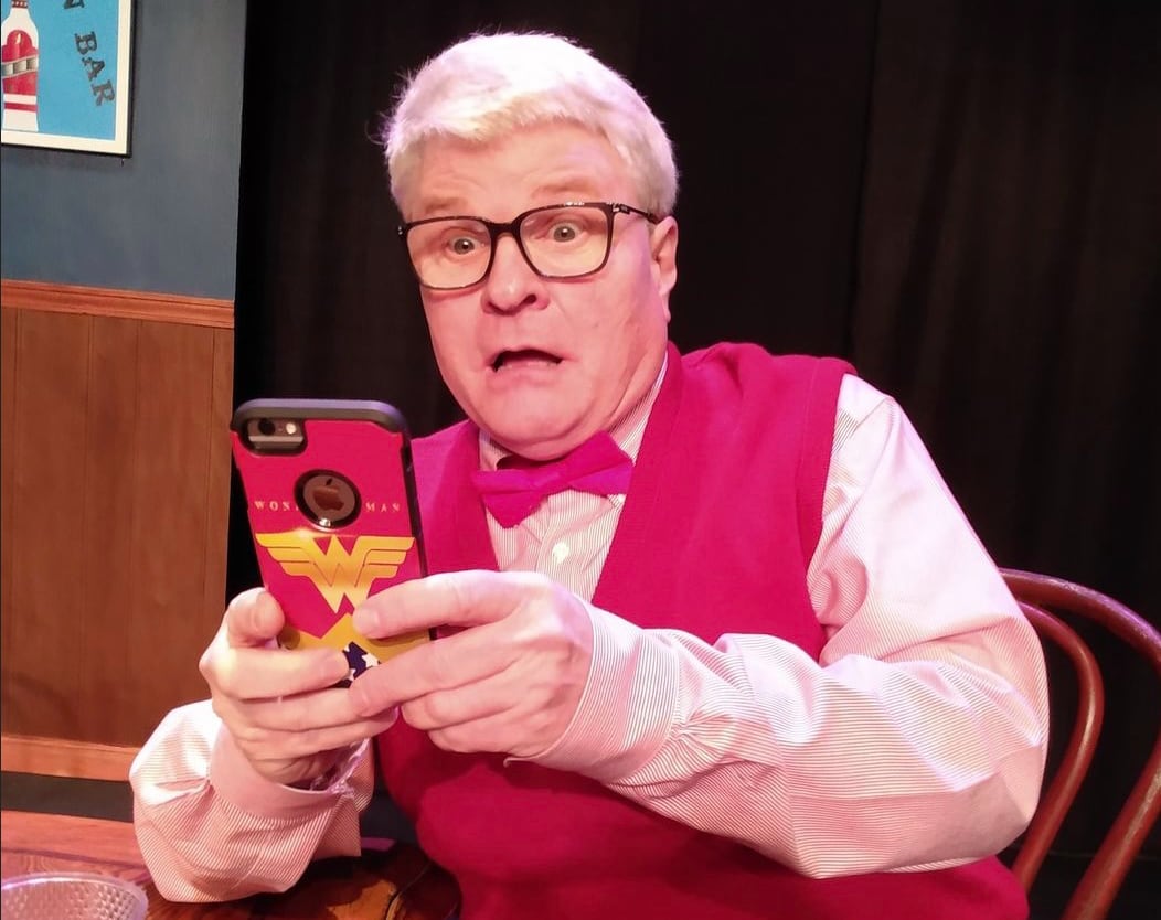 Ward dressed in red with glasses surprised at what he sees in his Wonder Woman phone